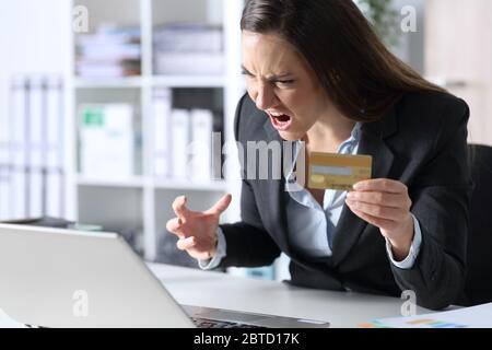 Wütende Exekutive Frau zahlt online mit Kreditkarte auf Laptop sitzt auf einem Schreibtisch im Büro Stockfoto