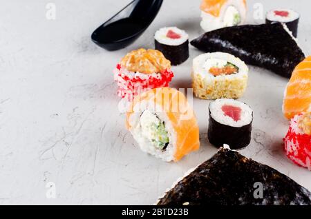 Verschiedene Sushi und Brötchen mit Sojasoße, Ingwer, Wasabi und Essstäbchen auf einem grauen Betontisch. Sushi-Menü. Lieferservice Japanisches Essen. Stockfoto