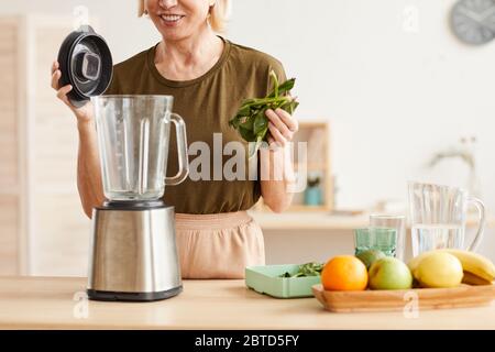 Nahaufnahme der reifen Frau, die Spinat in den Mixer sie wird einen gesunden Cocktail zu machen Stockfoto
