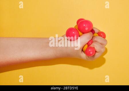 Hand Squishing eine bunte Spielzeugkugel eines Kindes über einem hellen gelben Hintergrund mit Schatten und Kopie Raum gehören Stockfoto