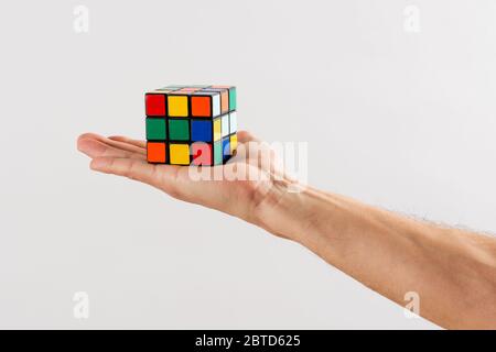 Mann hält ein ungelöstes Rubiks Cube-Puzzle auf der Handfläche seiner Hand über eine weiße Wand Hintergrund gestreckt Stockfoto