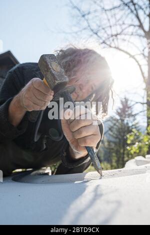 Niedrige Winkelansicht eines älteren Künstlers, der Kurven in weißem Stein mit großer Präzision schnitzen, mit Meißel und einem Schlägel. Stockfoto