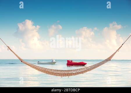 Leere Hängematte unter hohen Palmen am tropischen Strand und Schnellboot Stockfoto