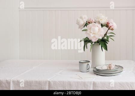 Stilisierte Stock Foto. Feminine Hochzeit oder Geburtstag Tischkomposition mit Blumenstrauß. Rosa Pfingstrosen Blumen, Tasse Kaffee, Teller und Seidenbänder, Stockfoto