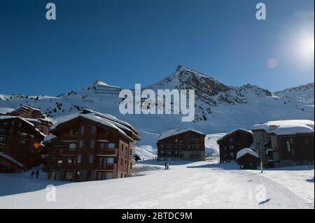 Wintersonne im Skigebiet Belle Plagne hoch in den Savoyer alpen, Frankreich. Eine Skipiste führt durch das Dorfzentrum. Stockfoto