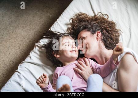 Eine Mutter und ihre Tochter schauen sich zärtlich an, während sie einen Moment der Intimität haben, während sie auf dem Bett liegen Stockfoto