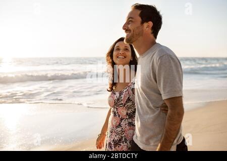 Liebevolles junges Paar, das zusammen an einem Sandstrand entlang läuft Stockfoto