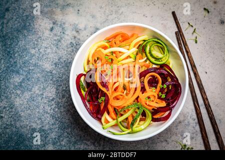 Gemüsennudeln - Zucchini, Rüben und Möhren in einer Schüssel, dunkler Hintergrund. Rohes veganes Essen. Stockfoto