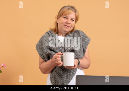 Ruhige seniorr Frau in grauem Schal mit Tasse Tee Blick auf die Kamera Stockfoto