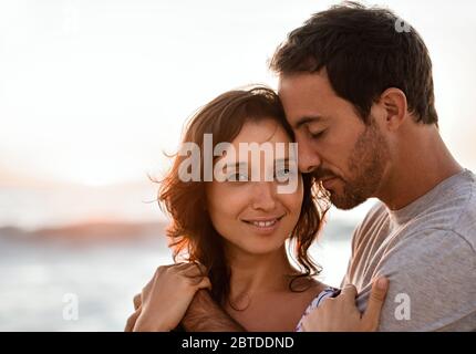 Lächelnde junge Frau, die in den Armen ihres Mannes an einem Strand steht Stockfoto