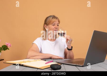 Schöne ältere Frau, die mit Freunden auf ihrem Laptop plaudert, während sie zu Hause ein Glas Wein genießt Stockfoto
