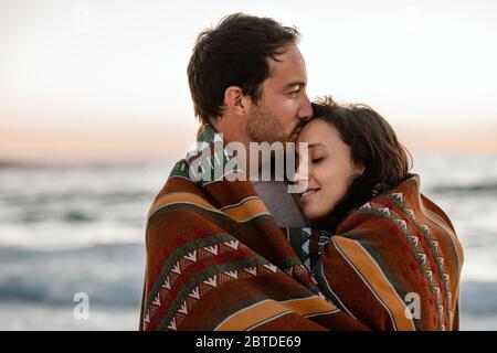 Liebevolles Paar, das auf einem Strand in einer Decke gewickelt steht Stockfoto