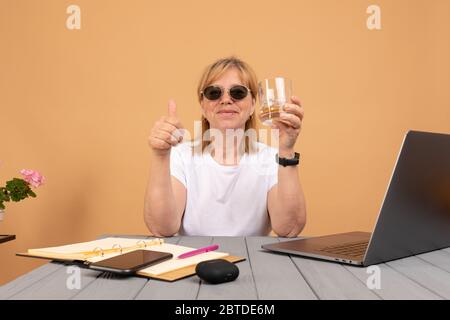 Glücklich betrunken ältere Frau in Sonnenbrille trinken Whisky und arbeiten an ihrem Computer Stockfoto