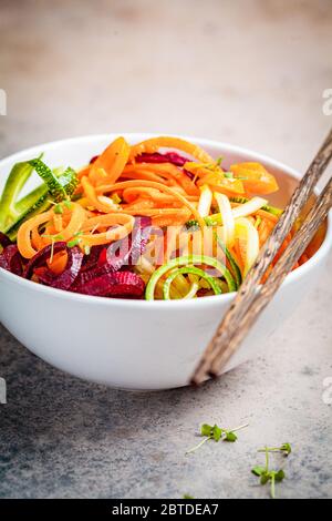 Gemüsennudeln - Zucchini, Rüben und Möhren in einer Schüssel, dunkler Hintergrund. Rohes veganes Essen. Stockfoto