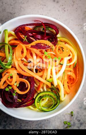 Gemüsennudeln - Zucchini, Rüben und Möhren in einer Schüssel, dunkler Hintergrund. Rohes veganes Essen. Stockfoto