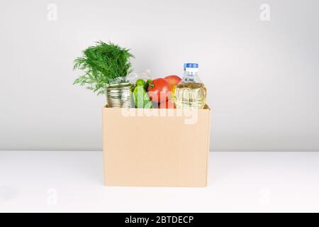 Spendenbox mit Lebensmitteln, offene Karteikarte mit Öl, Äpfeln, Gurken, Tomaten und Konserven. Stockfoto