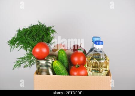 Spendenbox mit Lebensmitteln, offene Karteikarte mit Öl, Äpfeln, Gurken, Tomaten und Konserven. Stockfoto