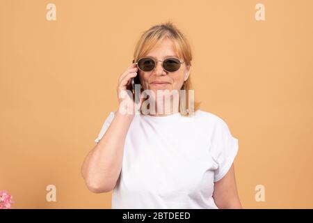 Telefongespräch. Positive gealterte Frau in schwarzer Sonnenbrille lächelt beim Telefonieren Stockfoto