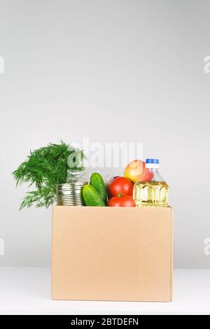 Spendenbox mit Lebensmitteln, offene Karteikarte mit Öl, Äpfeln, Gurken, Tomaten und Konserven. Stockfoto