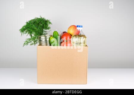 Spendenbox mit Lebensmitteln, offene Karteikarte mit Öl, Äpfeln, Gurken, Tomaten und Konserven. Stockfoto