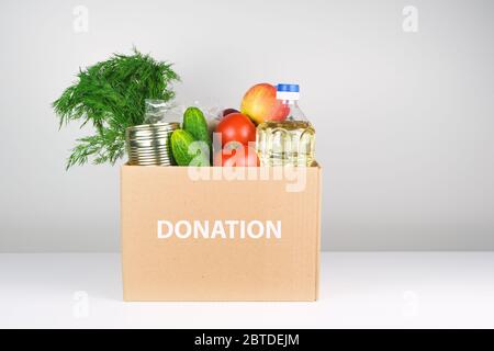 Spendenbox mit Lebensmitteln, offene Karteikarte mit Öl, Äpfeln, Gurken, Tomaten und Konserven. Copyspace. Stockfoto