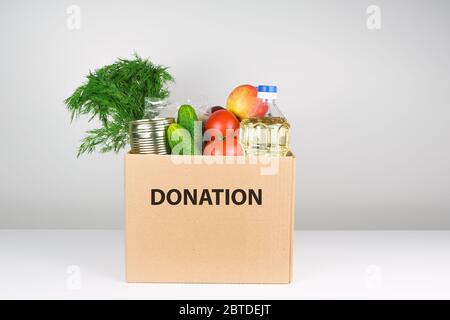 Spendenbox mit Lebensmitteln, offene Karteikarte mit Öl, Äpfeln, Gurken, Tomaten und Konserven. Copyspace. Stockfoto