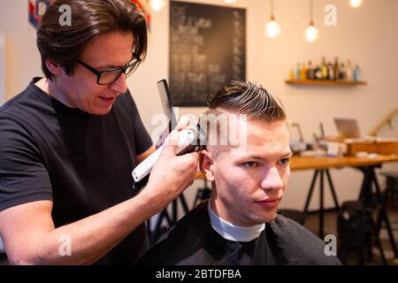 Barbier trimmt die Haare eines jungen Mannes mit einem Rasiermesser in seinem Friseursalon Stockfoto