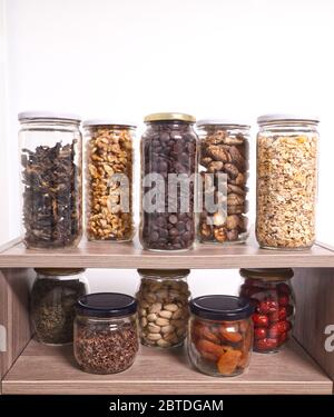 Lagerung von Schüttgütern in Gläsern: Trockene Pilze, Müsli, Schokolade, Nüsse, Datteln, Pistazien, aromatische Kräuter. Konzept ohne Verschwendung. Stockfoto