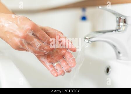 Mann oder Frau wäscht sich die Hände mit Seife, während sie im Badezimmer am Waschbecken steht. Stockfoto