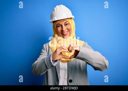Mittelalter Brünette Architektin Frau mit muslimischen traditionellen Hijab und Sicherheit Helm lächelnd in der Liebe zeigt Herz Symbol und Form mit den Händen. Ro Stockfoto