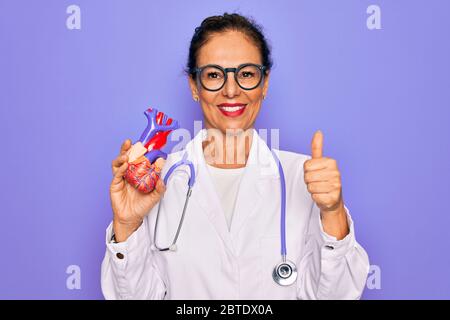 Mittlere Alter Senior Kardiologe Arzt Frau, die professionelle Kardiologie Herz glücklich mit großen Lächeln tun ok Zeichen, Daumen hoch mit den Fingern, ausgezeichnet Stockfoto