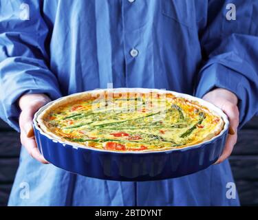 Eine Frau hält frisch gebackene Quiche mit Lachs Spargel Käsefüllung, Nahaufnahme, horizontale Ansicht Stockfoto