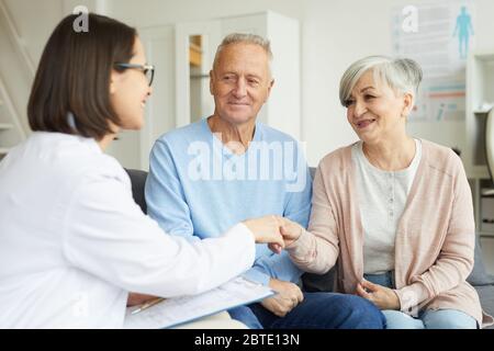 Porträt des modernen älteren Paar schüttelt die Hände mit Ärztin und lächelt beim Besuch der Privatklinik Stockfoto