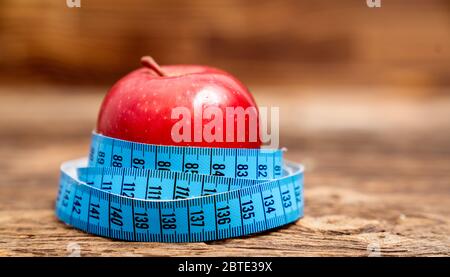 Nahaufnahme frischer roter Apfel mit Maßband isoliert auf Holzhintergrund. Schlanke Ernährung und Essen für die Gesundheit Stockfoto