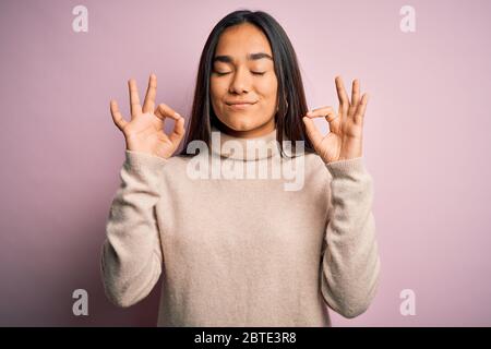 Junge schöne asiatische Frau mit lässigen Rollkragen Pullover über rosa Hintergrund entspannen und lächeln mit geschlossenen Augen tun Meditation Geste mit Fi Stockfoto