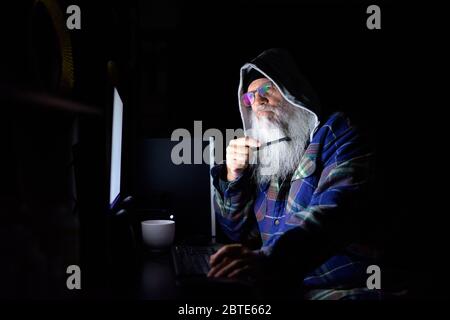 Reife bärtige Hipster Mann Kämmen Bart während der Arbeit Überstunden zu Hause im Dunkeln Stockfoto