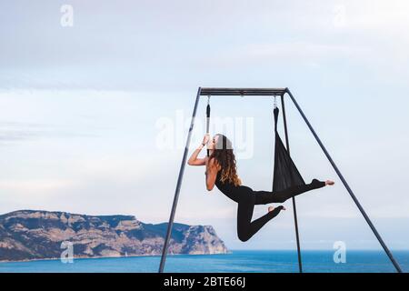 Frau Praxis akrobatisches fliegen Tanz Yoga im Freien mit Ausblick auf das Meer und die Berge. Gesunder Lebensstil Konzept. Weibliche Sport. Akrobatische Gymnastik. Stockfoto