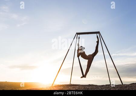 Schlanke Frau üben fliegen Tanz akrobatischen Yoga Posen in der Hängematte im Freien bei Sonnenuntergang. Sport und Wohlbefinden Konzept. Gesunde Lebensweise. Stockfoto