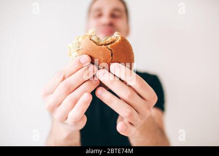 Junger Mann isoliert auf weißem Hintergrund. Guy halten beigen Cheeseburger in den Händen und zeigen es vor der Kamera. Unscharf oder unscharf. Zufrieden glücklich Stockfoto