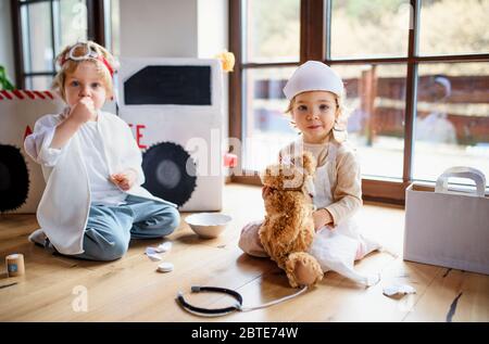 Zwei kleine Kinder mit Arztuniformen zuhause, spielend. Stockfoto