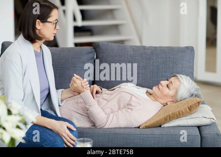 Seitenansicht Porträt der älteren Frau auf der Couch mit jungen Tochter, die ihre Hand und Unterstützung Mutter, Kopie Raum Stockfoto