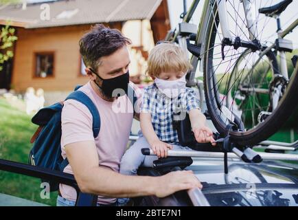 Vater mit kleinem Sohn, der Fahrräder auf dem Autodach für die Reise legt, Gesichtsmasken trägt. Stockfoto