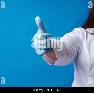 medic Frau im weißen Mantel, mit blauen medizinischen Latexhandschuhen an den Händen, zeigt wie Geste mit seiner rechten Hand, Genehmigung Konzept Stockfoto