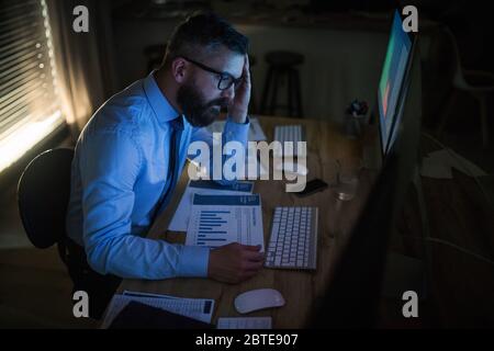 Frustrierter Geschäftsmann mit Computer an der Rezeption, der spät arbeitete. Konzept der Finanzkrise. Stockfoto