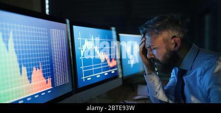 Frustrierter Geschäftsmann mit Computer an der Rezeption, der spät arbeitete. Konzept der Finanzkrise. Stockfoto