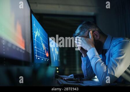 Frustrierter Geschäftsmann mit Computer an der Rezeption, der spät arbeitete. Konzept der Finanzkrise. Stockfoto