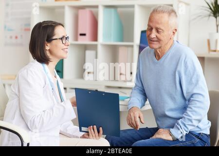 Porträt einer lächelnden Ärztin, die dem Senior Patient während der Konsultation in der Klinik das Klemmbrett zeigt Stockfoto