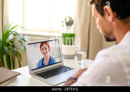 Mann mit Videoanruf mit Arzt auf Laptop zu Hause, Online-Beratung Konzept. Stockfoto