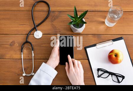 Ärztin tippt auf Smartphone mit leerem Bildschirm auf Holztisch Stockfoto