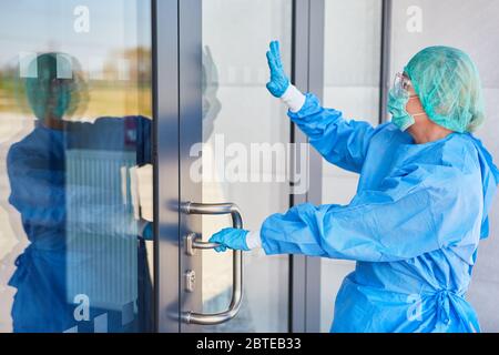 Mitarbeiter in Schutzkleidung vor der Klinik geben Handzeichen an die Tür, bevor sie während der Covid-19-Pandemie eintreten Stockfoto